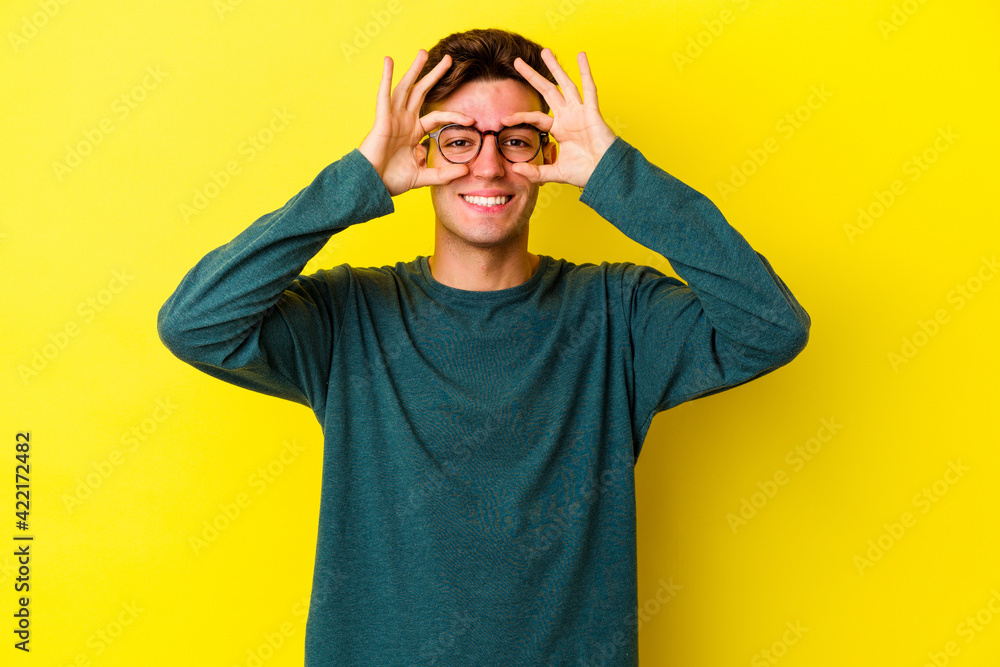 Young caucasian man isolated on yellow background excited keeping ok gesture on eye. Young caucasian man isolated on yellow background excited keeping ok gesture on eye.