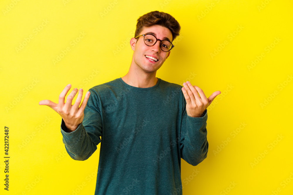 Young caucasian man isolated on yellow background pointing with finger at you as if inviting come closer. Young caucasian man isolated on yellow background pointing with finger at you as if inviting come closer.