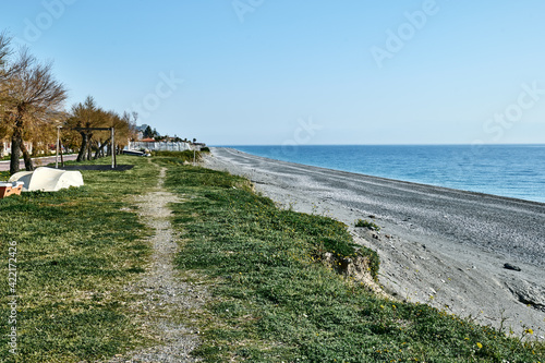 Promenade with palm trees near the winter beach of the Ionian Sea. The trees without leaves and the wooden boat at the shore of the Mediterranean sea. © Caterina Trimarchi