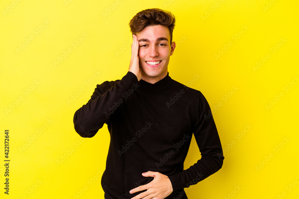 Young caucasian man isolated on yellow background laughs happily and has fun keeping hands on stomach. Young caucasian man isolated on yellow background laughs happily and has fun keeping hands on stomach.