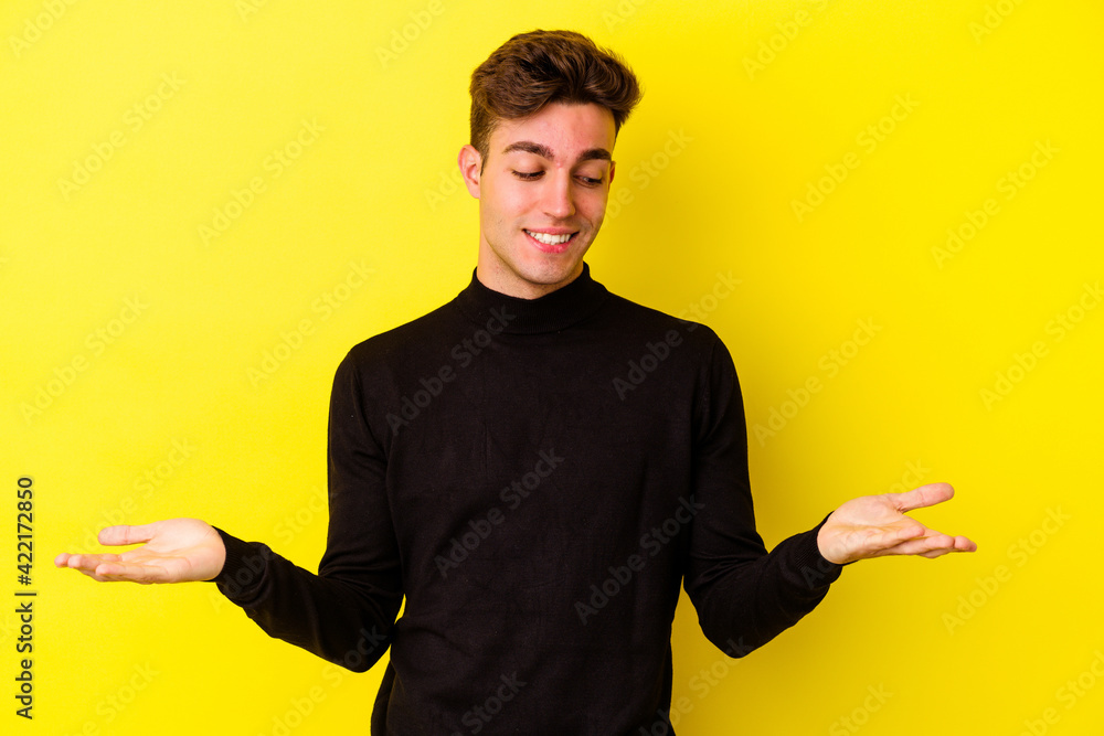 Fototapeta premium Young caucasian man isolated on yellow background holding something with palms, offering to camera.