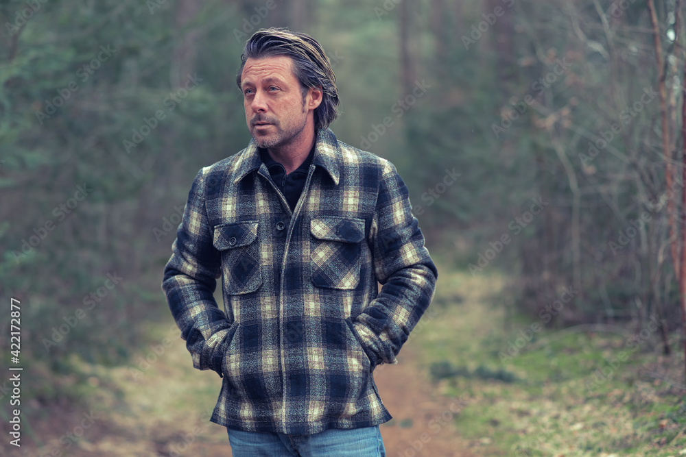 Blonde man in checkered coat walking on a path in a forest. Blonde man in checkered coat walking on a path in a forest.