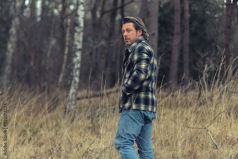 Obraz premium Man in checkered coat in field with tall yellow grass near a forest.