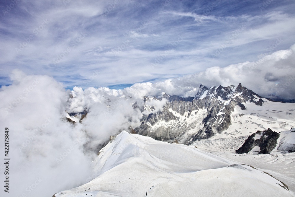 Obraz premium The mountain ranges are covered with snow and clouds. Snowy mountain peaks on a sunny winter day. Scenic Mountain landscape from the top of the mountain. Climbing mountain summits among the clouds.