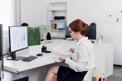 A young accountant in the office examines accounting financial tax reports in the office of a commercial company. Mockup monitor