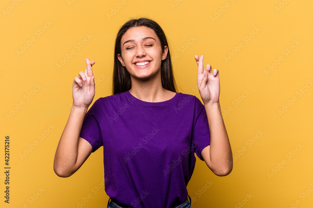 Young Indian woman isolated on yellow background crossing fingers for having luck Young Indian woman isolated on yellow background crossing fingers for having luck