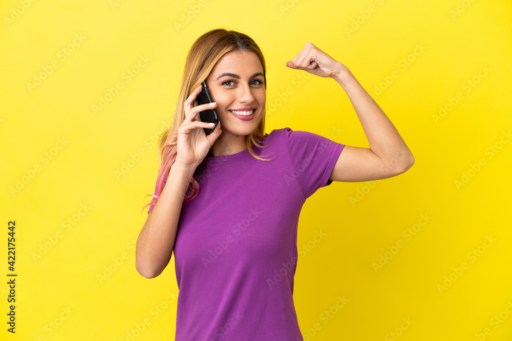 Fototapeta premium Young woman using mobile phone over isolated yellow background doing strong gesture