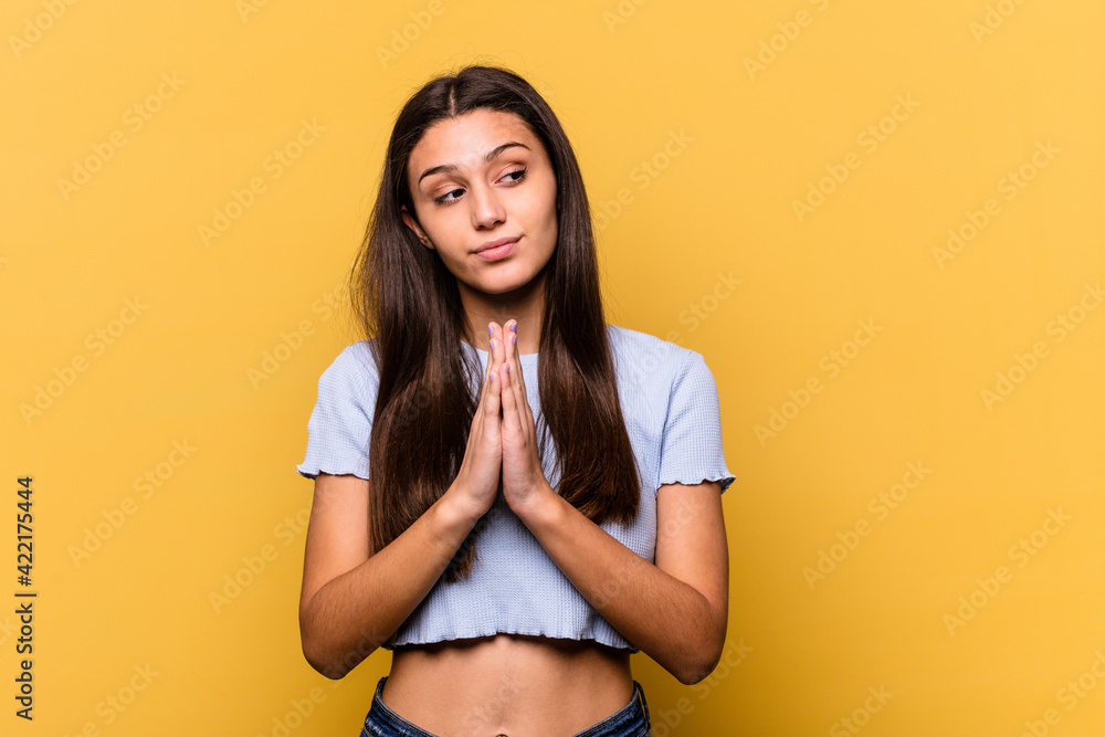 Obraz premium Young Indian woman isolated on yellow background praying, showing devotion, religious person looking for divine inspiration.