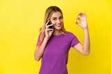 Young woman using mobile phone over isolated yellow background showing ok sign with fingers