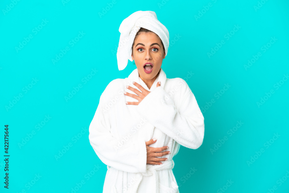Young woman in a bathrobe over isolated blue background surprised and shocked while looking right Young woman in a bathrobe over isolated blue background surprised and shocked while looking right