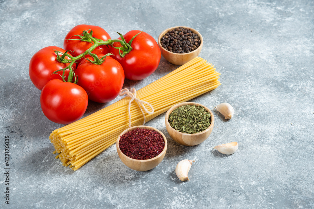 Raw spaghetti, spices and tomatoes on marble background Raw spaghetti, spices and tomatoes on marble background