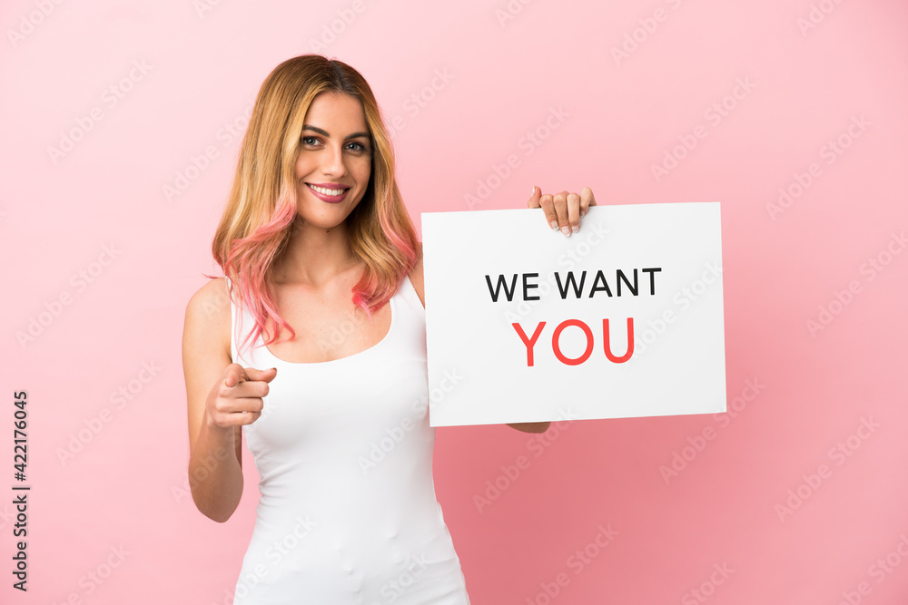 Young woman over isolated pink background holding We Want You board and pointing to the front Young woman over isolated pink background holding We Want You board and pointing to the front