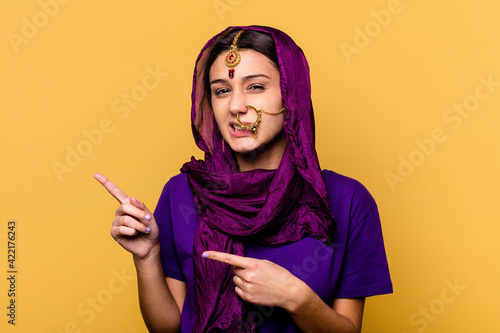 Young Indian woman wearing a traditional sari clothes isolated on yellow background shocked pointing with index fingers to a copy space.