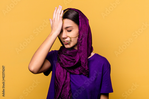 Young Indian woman wearing a traditional sari clothes isolated on yellow background forgetting something, slapping forehead with palm and closing eyes. © Asier
