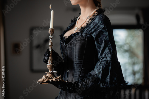 Fototapeta Beautiful woman in vintage black dress holding a candlestick