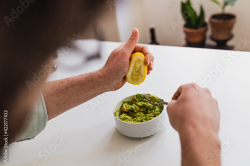Man preparing guacamole with a ripe avocado. Bright indoor ambient with a white color palette. Organic healthy food.