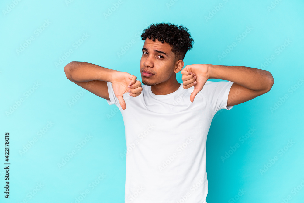 Young african american curly man isolated on blue showing thumb down, disappointment concept. Young african american curly man isolated on blue showing thumb down, disappointment concept.