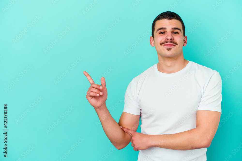 Young caucasian man isolated on blue background smiling cheerfully pointing with forefinger away. Young caucasian man isolated on blue background smiling cheerfully pointing with forefinger away.