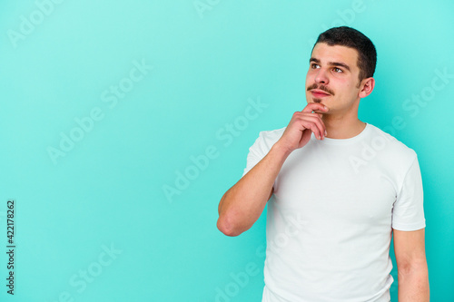 Young caucasian man isolated on blue background looking sideways with doubtful and skeptical expression.