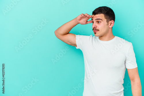 Young caucasian man isolated on blue background looking far away keeping hand on forehead.
