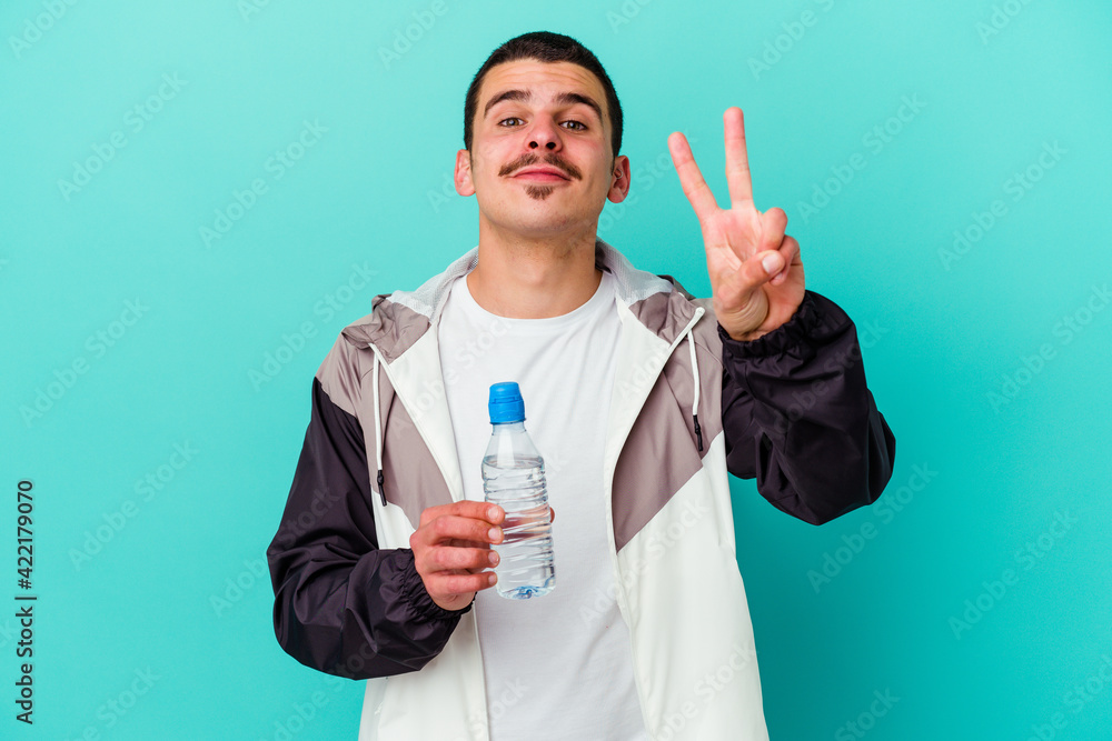 Young sporty caucasian man drinking water isolated on blue background showing number two with fingers. Young sporty caucasian man drinking water isolated on blue background showing number two with fingers.