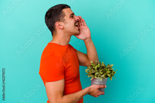 Young caucasian man holding a leaf isolated on blue background shouting and holding palm near opened mouth.