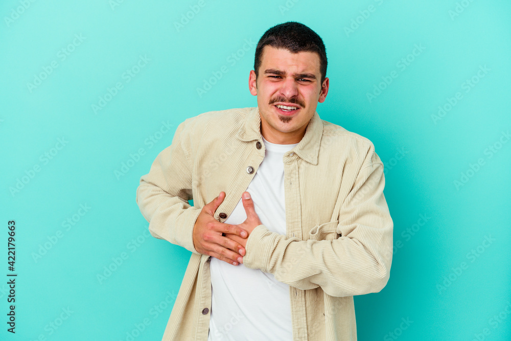 Young caucasian man isolated on blue background having a liver pain, stomach ache. Young caucasian man isolated on blue background having a liver pain, stomach ache.