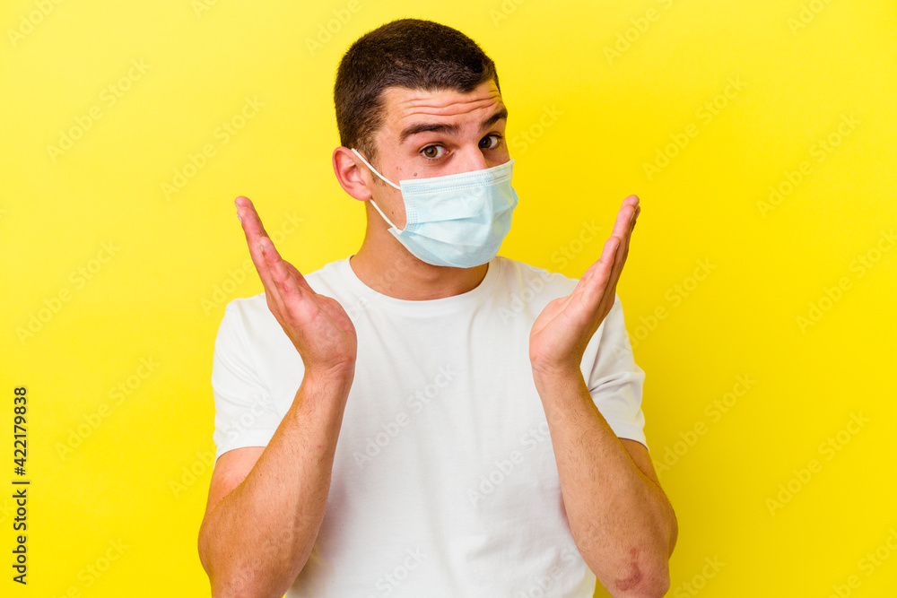 Young caucasian man wearing a protection for coronavirus isolated on yellow background surprised and shocked.