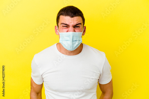 Young caucasian man wearing a protection for coronavirus isolated on yellow background screaming very angry and aggressive. © Asier