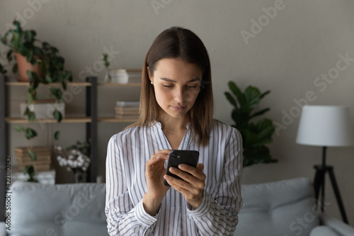 Close up focused woman using smartphone looking at screen, browsing apps, surfing internet, young female holding phone, chatting or shopping online, spending leisure time, standing at home