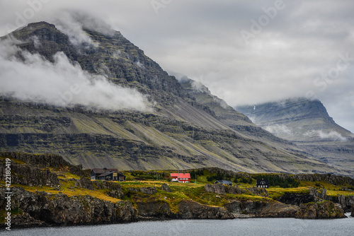 The cloud shrouded mountains of Berufjordur fjord tower above a farm near Djupivogur village on the East Fjords region of East Iceland. photo