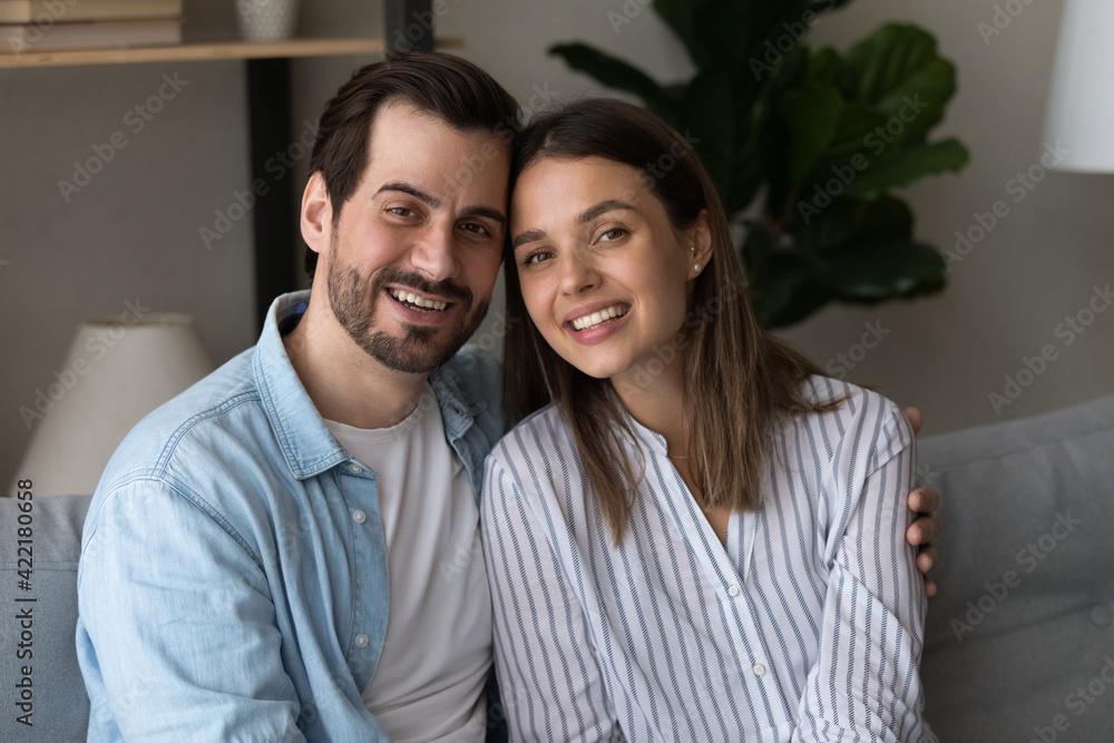 Head shot portrait smiling couple family hugging, looking at camera, sitting on couch at home, happy woman and man making video call to relatives or friends, positive bloggers shooting vlog Head shot portrait smiling couple family hugging, looking at camera, sitting on couch at home, happy woman and man making video call to relatives or friends, positive bloggers shooting vlog