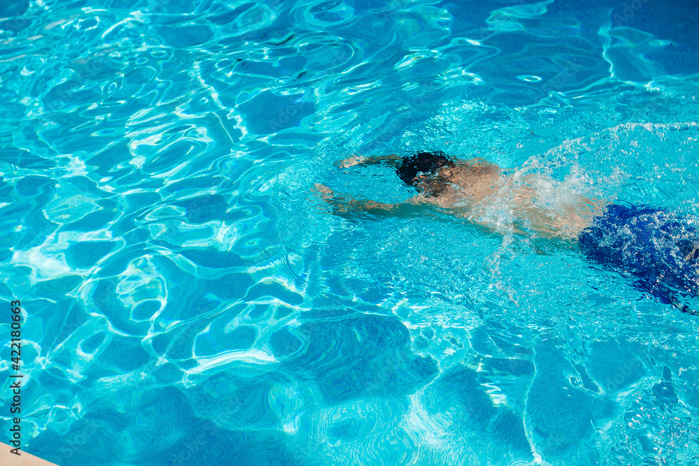 Young handsome man swims in a pool of blue water on a sunny summer day. Summer background