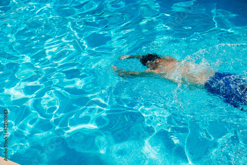 Young handsome man swims in a pool of blue water on a sunny summer day. Summer background