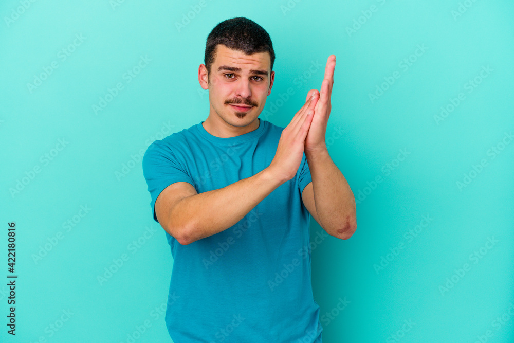 Young caucasian man isolated on blue background feeling energetic and comfortable, rubbing hands confident. Young caucasian man isolated on blue background feeling energetic and comfortable, rubbing hands confident.