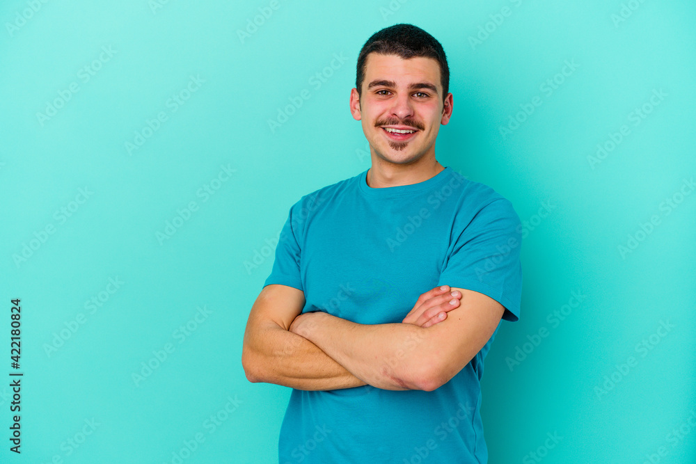 Young caucasian man isolated on blue background who feels confident, crossing arms with determination. Young caucasian man isolated on blue background who feels confident, crossing arms with determination.