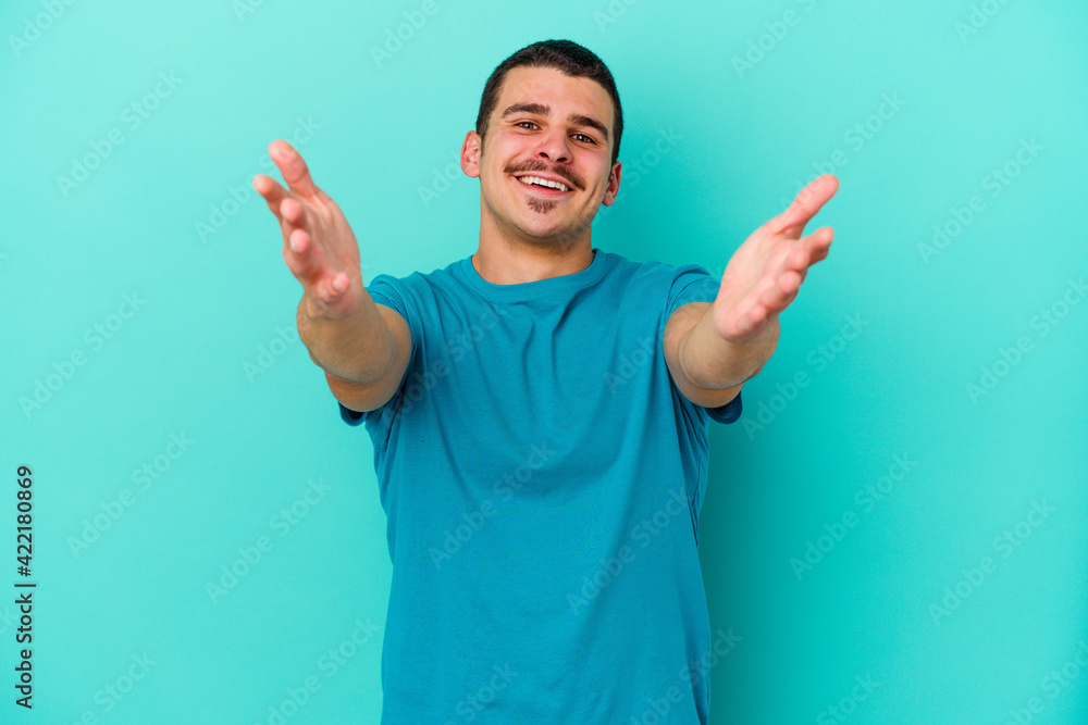 Young caucasian man isolated on blue background feels confident giving a hug to the camera. Young caucasian man isolated on blue background feels confident giving a hug to the camera.