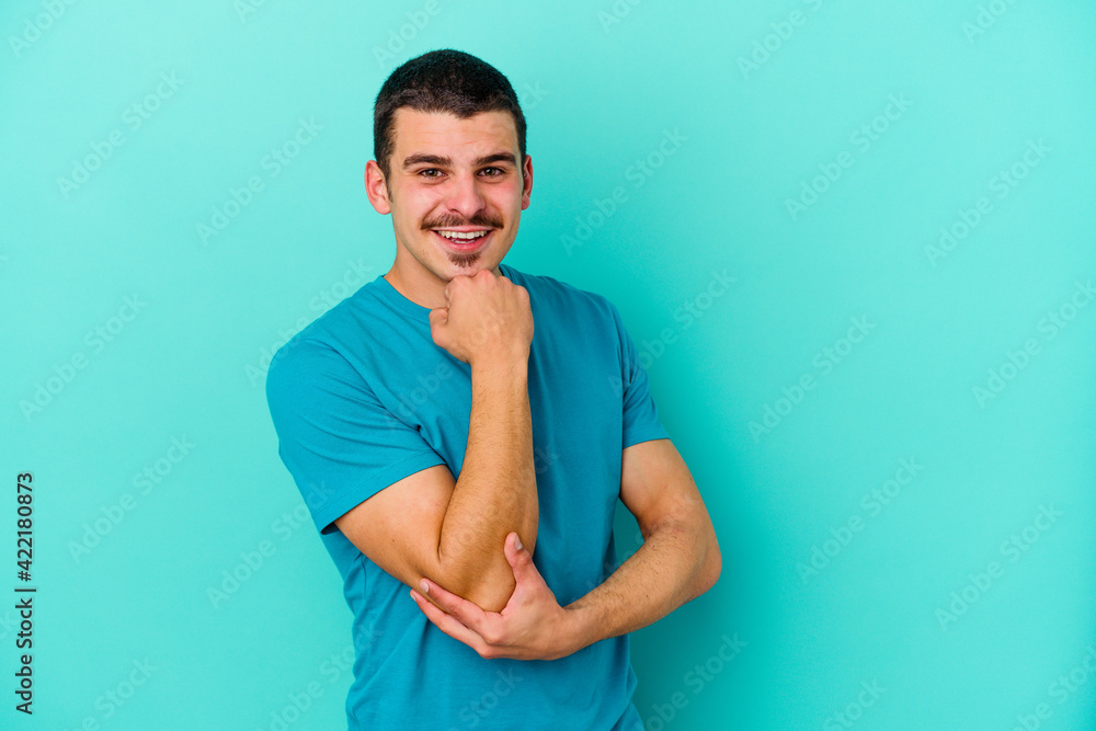 Young caucasian man isolated on blue background smiling happy and confident, touching chin with hand. Young caucasian man isolated on blue background smiling happy and confident, touching chin with hand.