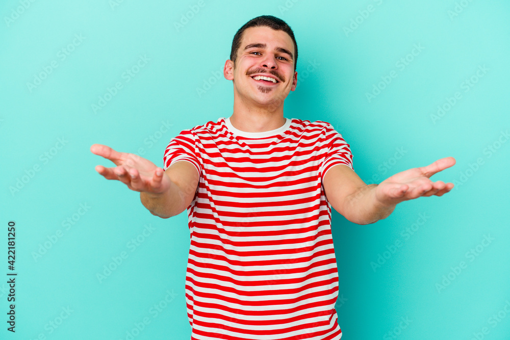 Young caucasian man isolated on blue background makes scale with arms, feels happy and confident. Young caucasian man isolated on blue background makes scale with arms, feels happy and confident.