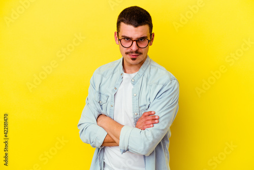 Young caucasian cool man isolated on yellow background frowning face in displeasure, keeps arms folded.