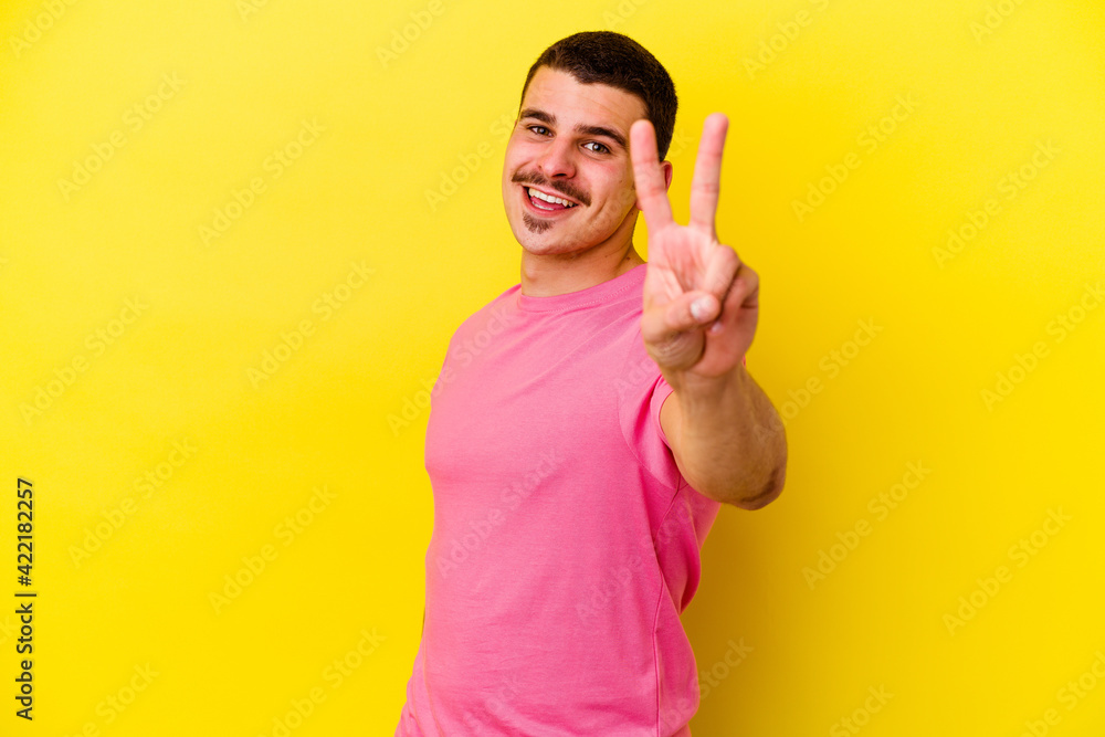 Young caucasian cool man isolated on yellow background joyful and carefree showing a peace symbol with fingers. Young caucasian cool man isolated on yellow background joyful and carefree showing a peace symbol with fingers.