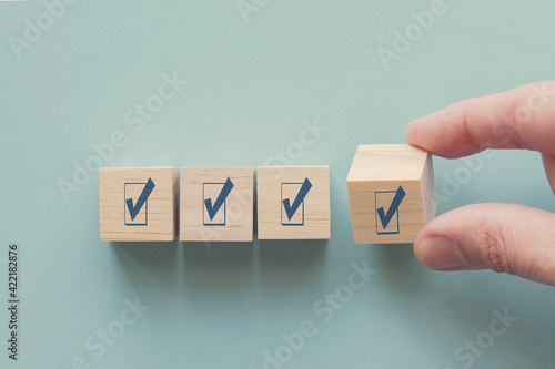 Hand holding wooden block with tick mark, satisfaction survey ,mental health assessment, checklist business, project tracking, goal tracker, task completion concept photo