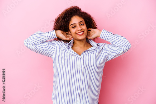 Young african american woman isolated on pink background stretching arms, relaxed position. © Asier