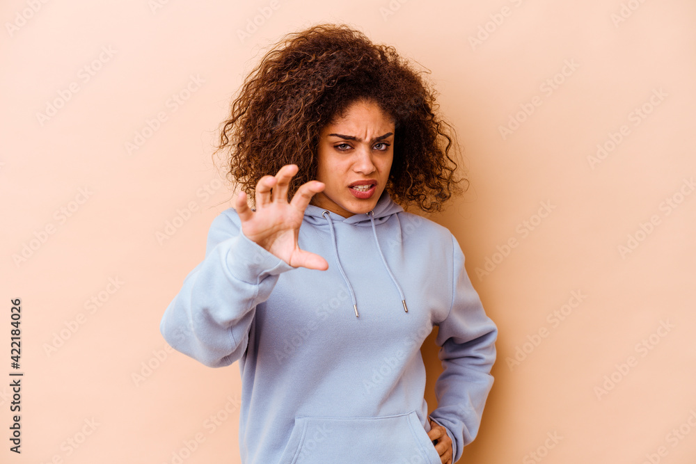 Young african american woman isolated on beige background showing claws imitating a cat, aggressive gesture. Young african american woman isolated on beige background showing claws imitating a cat, aggressive gesture.