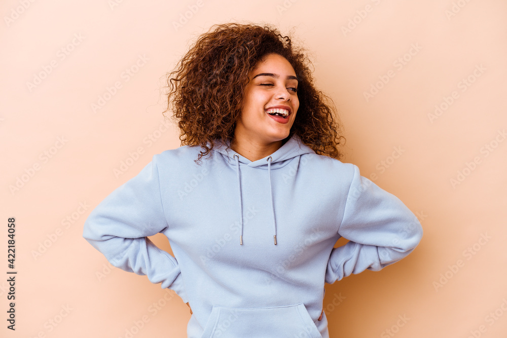 Fototapeta premium Young african american woman isolated on beige background laughs and closes eyes, feels relaxed and happy.