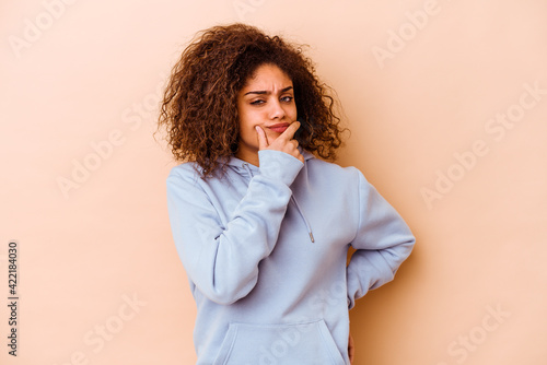 Young african american woman isolated on beige background contemplating, planning a strategy, thinking about the way of a business. © Asier