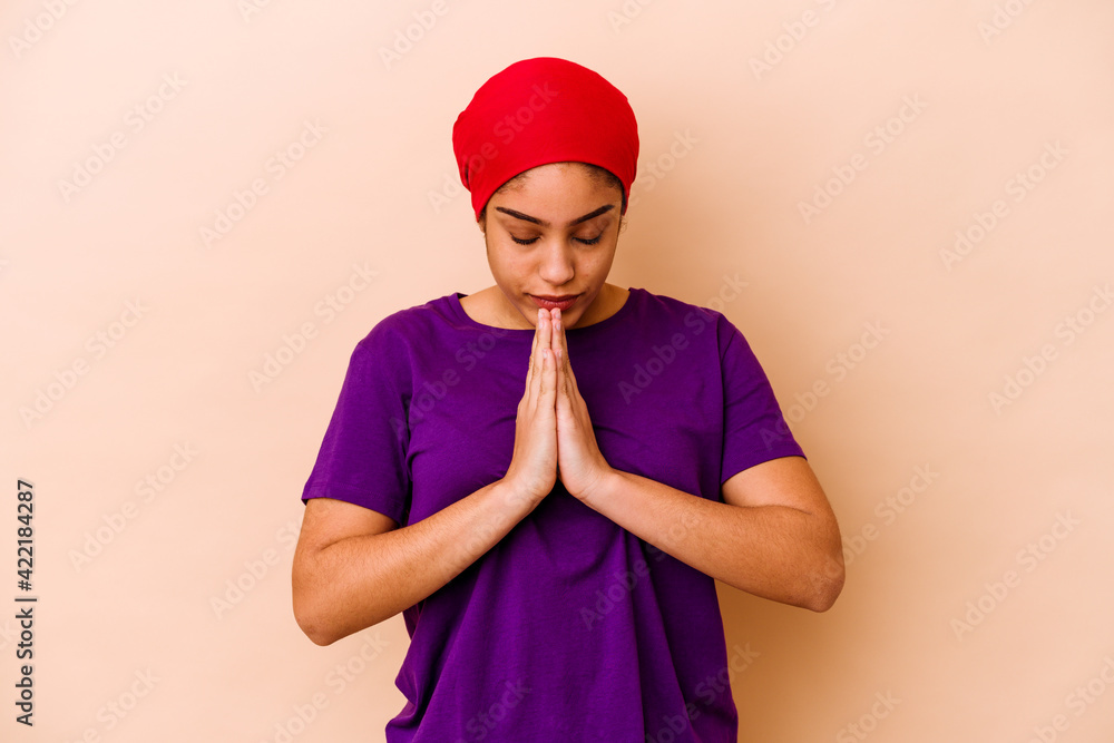 Young african american woman isolated on beige background praying, showing devotion, religious person looking for divine inspiration. Young african american woman isolated on beige background praying, showing devotion, religious person looking for divine inspiration.