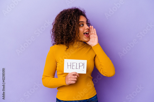 Young African American woman holding a Help placard isolated on purple background shouting and holding palm near opened mouth.