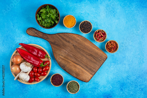 Various spices around wooden board with plate of vegetables