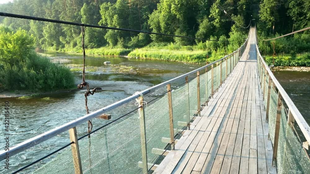 Swaying Rope Bridge Hanging wooden swaying bridge on steel ropes across the river. Plank ...